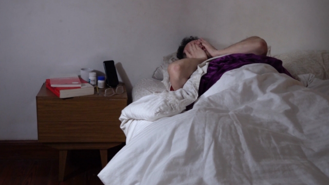 Muškarac leži u krevetu u mračnoj sobi, umoran i nervozan, pokriva lice rukama jer ne može da zaspi zbog nesanice