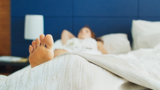 Žena leži budna u krevetu sa ispruženom nogom